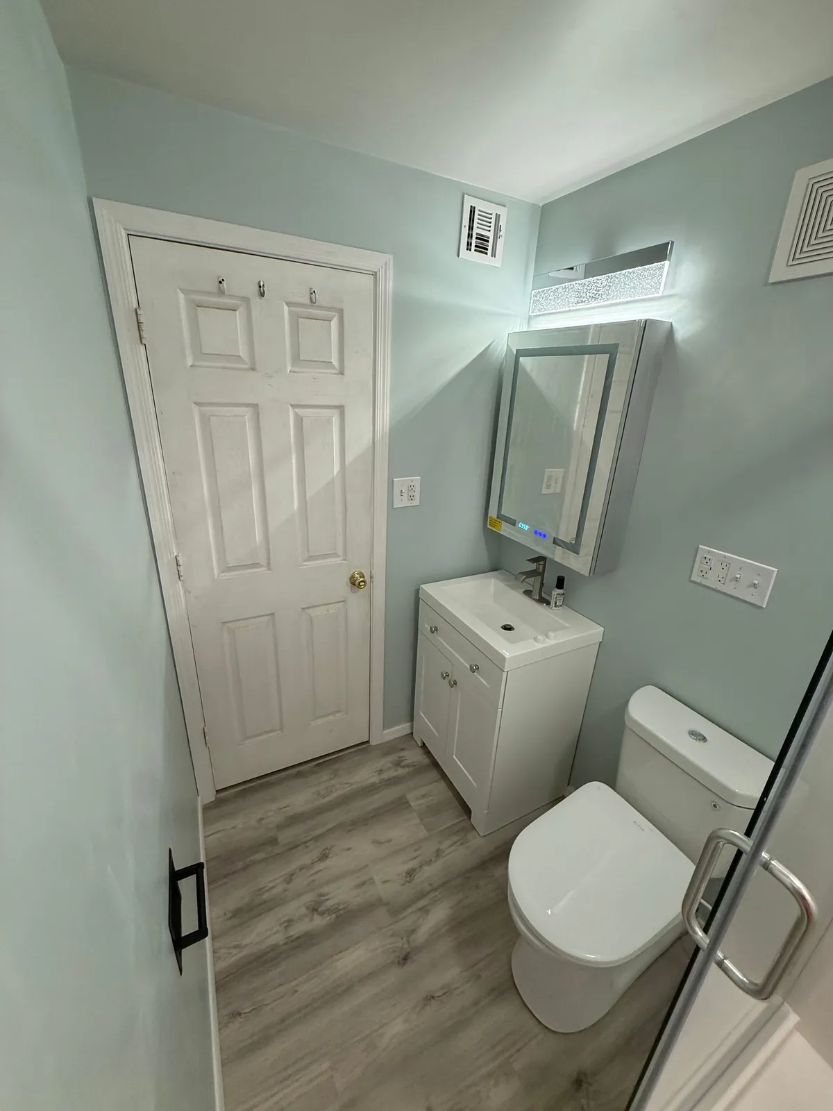 Remodeled bathroom with new vanity, lighted mirror cabinet, and plank flooring
